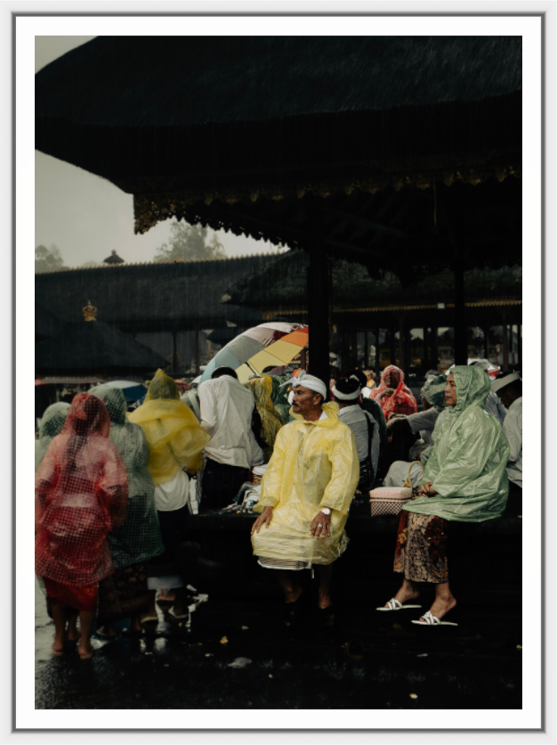 People in raincoats and umbrellas waiting under a shelter on a rainy day.