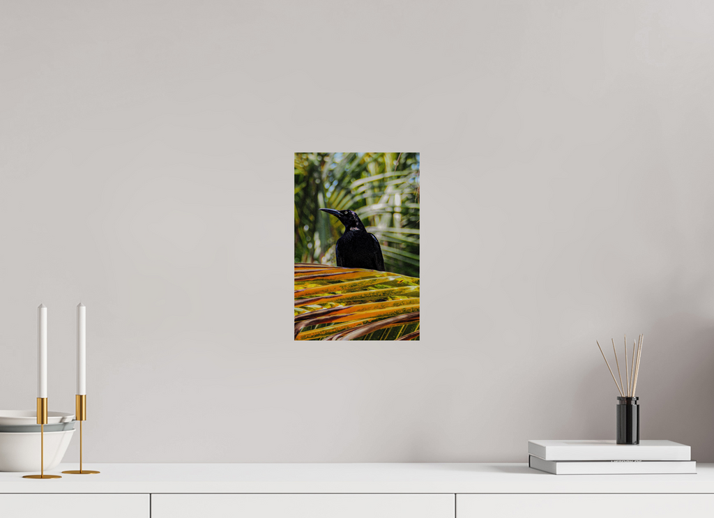 Wall art of a black bird on a branch with green leaves on a gray wall above a white surface.