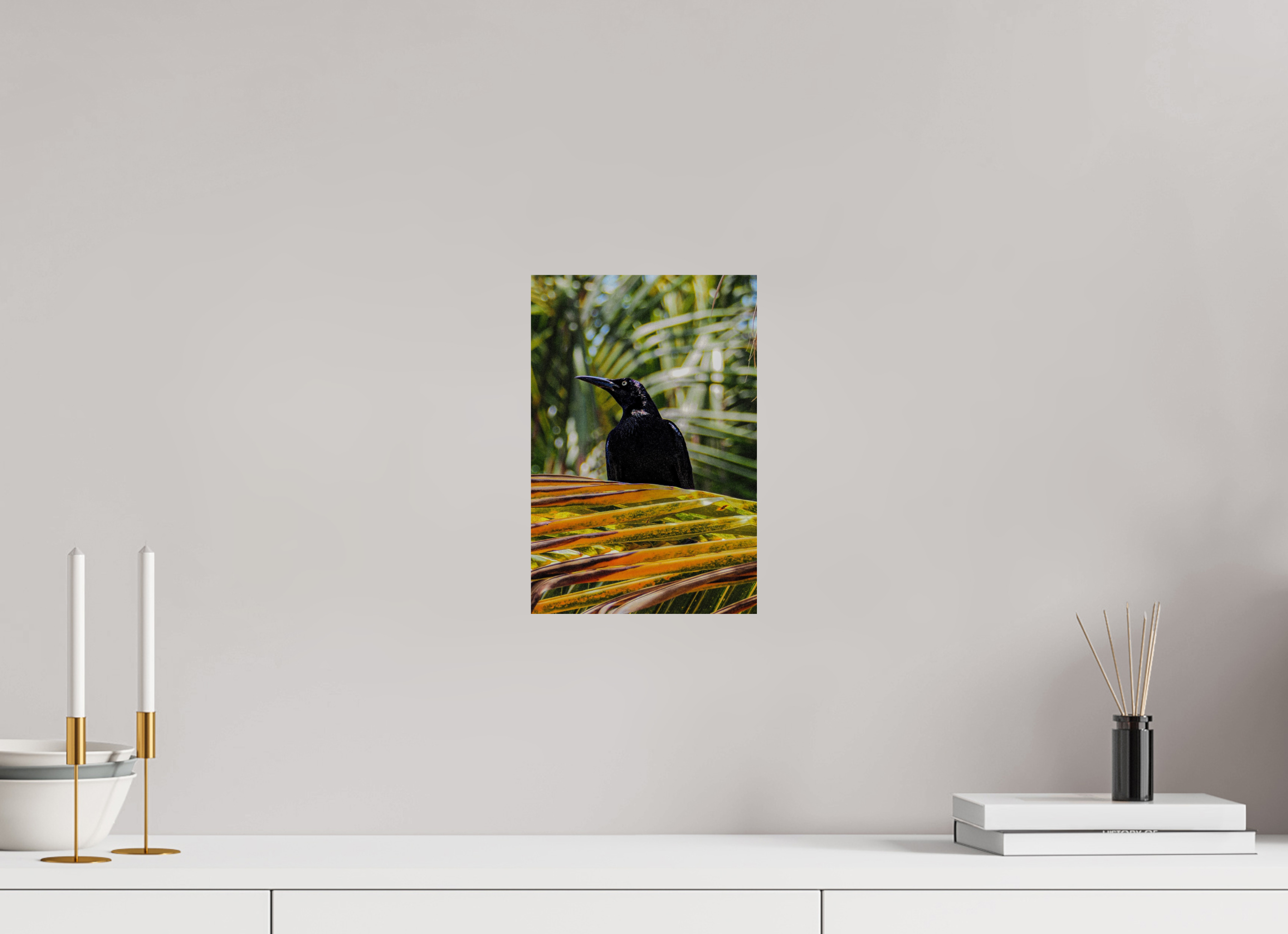 Wall art of a black bird on a branch with green leaves on a gray wall above a white surface.