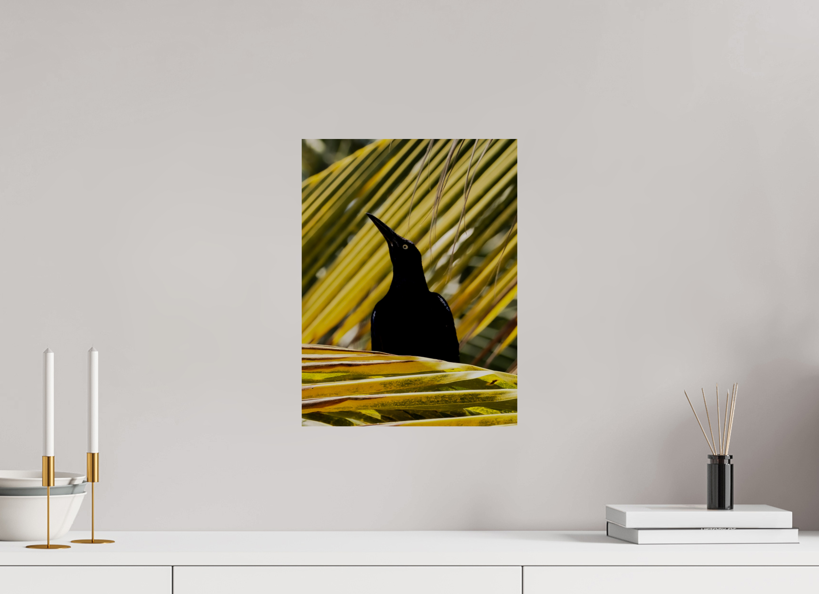 Framed artwork of a black bird on a yellow leaf against a white wall with decorative items on a shelf.