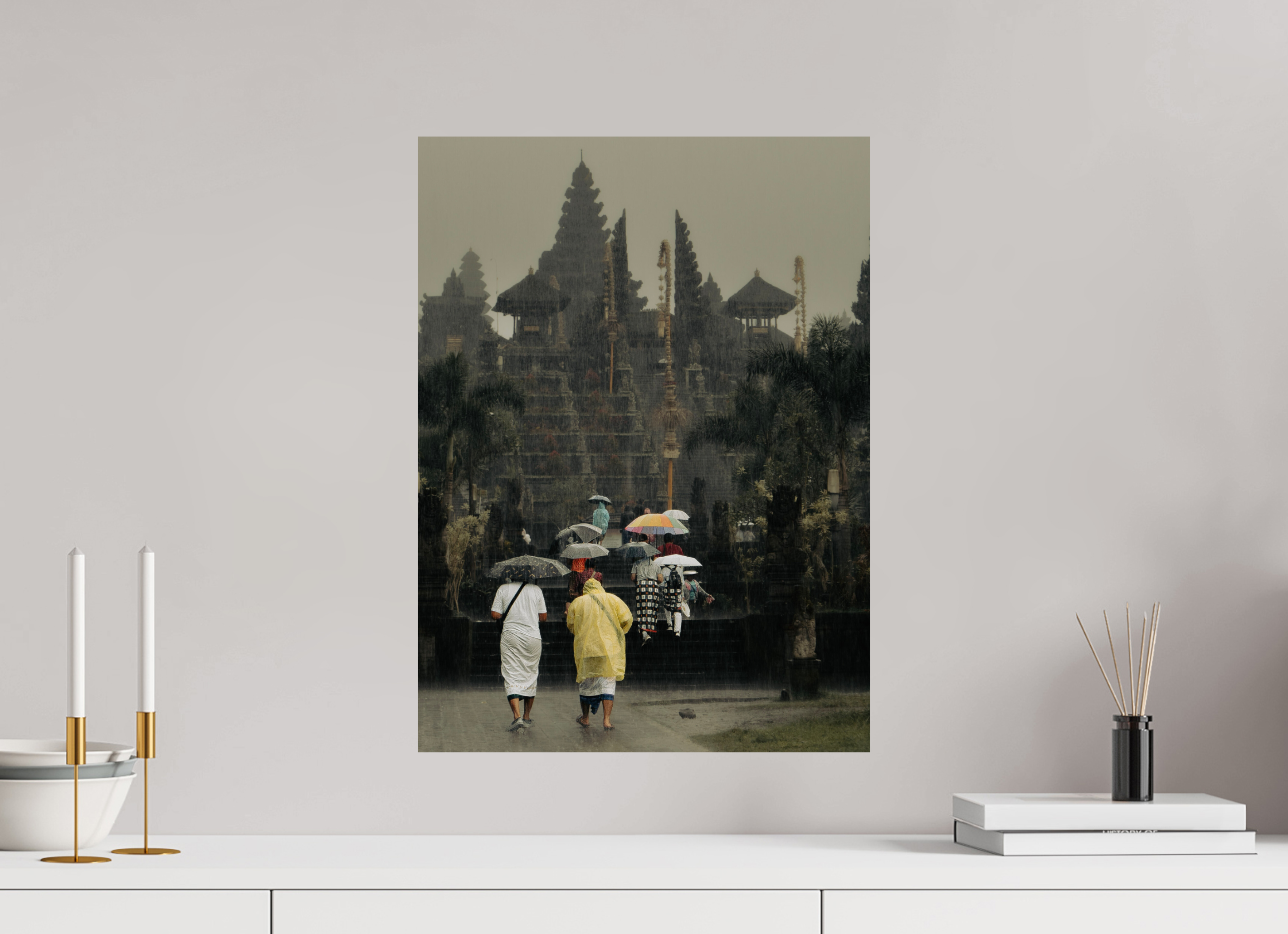 Framed artwork of people with umbrellas walking in a park, displayed on a wall above a white surface.