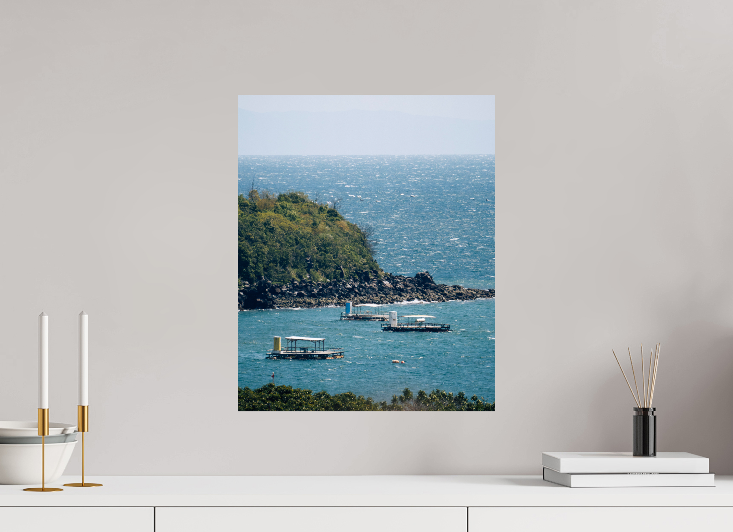Wall art of a coastal scene with boats, displayed on a wall above a white surface with decorative items.