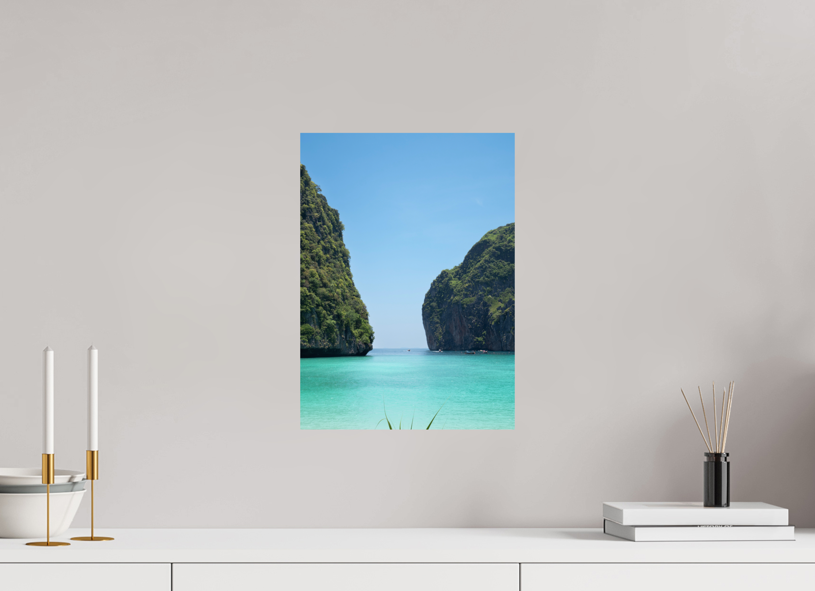 Framed photograph of a tropical island scene on a wall above a white surface with decorative items.