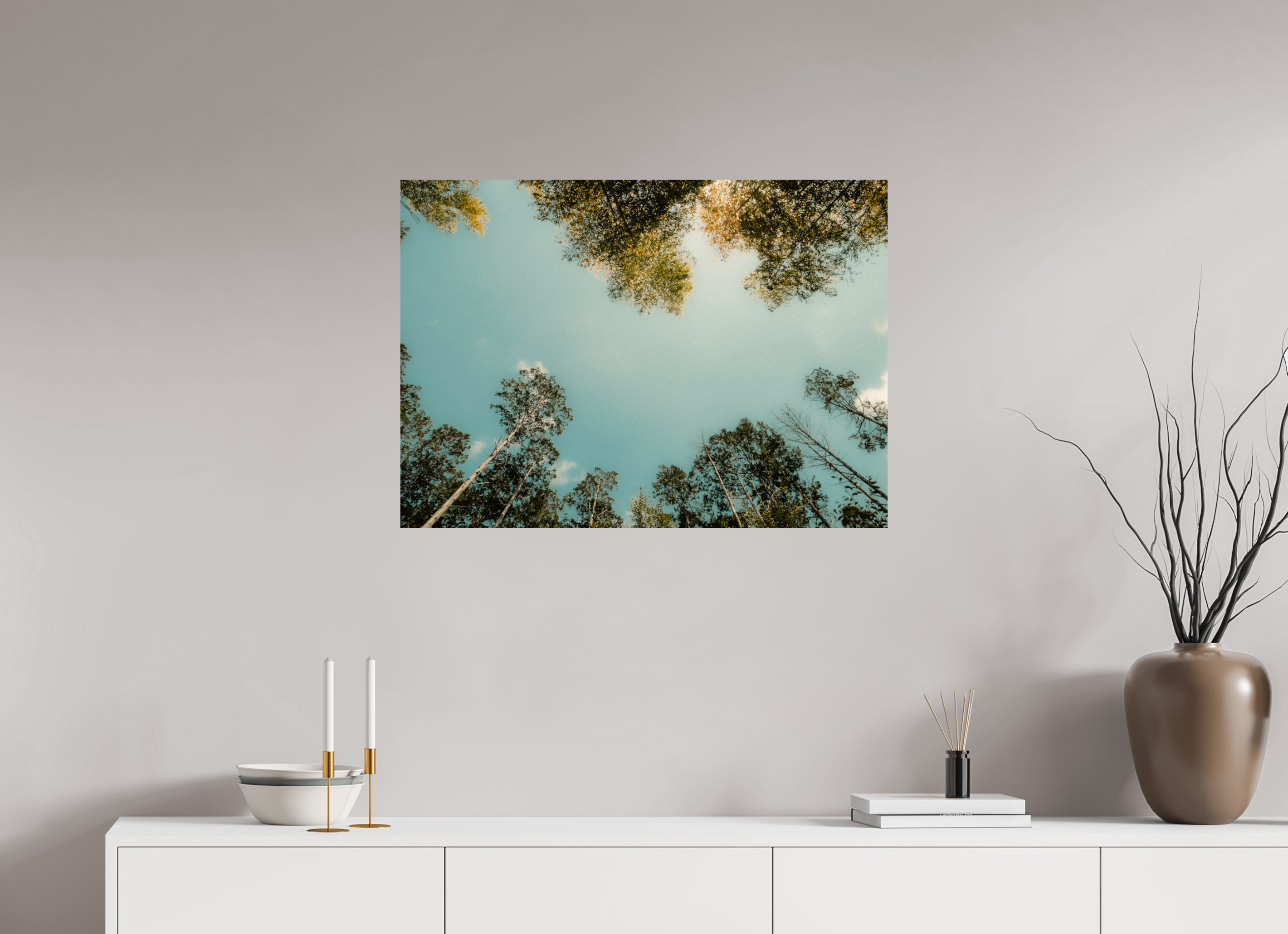 Framed nature print of trees against a blue sky on a wall above a white console table.