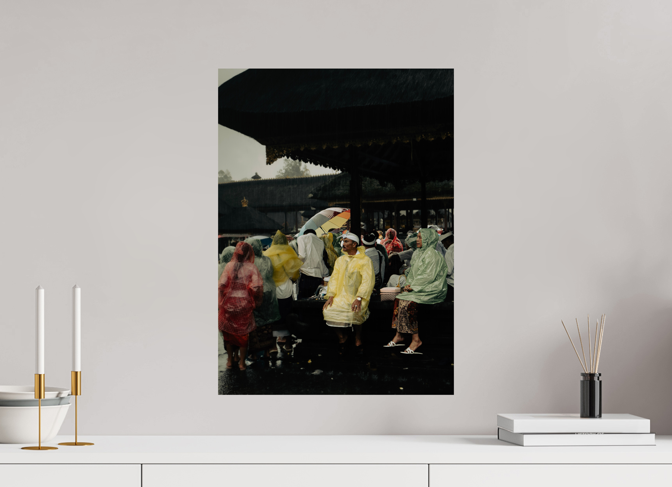 Framed photograph of people in raincoats on a wall above a white shelf with decorative items.