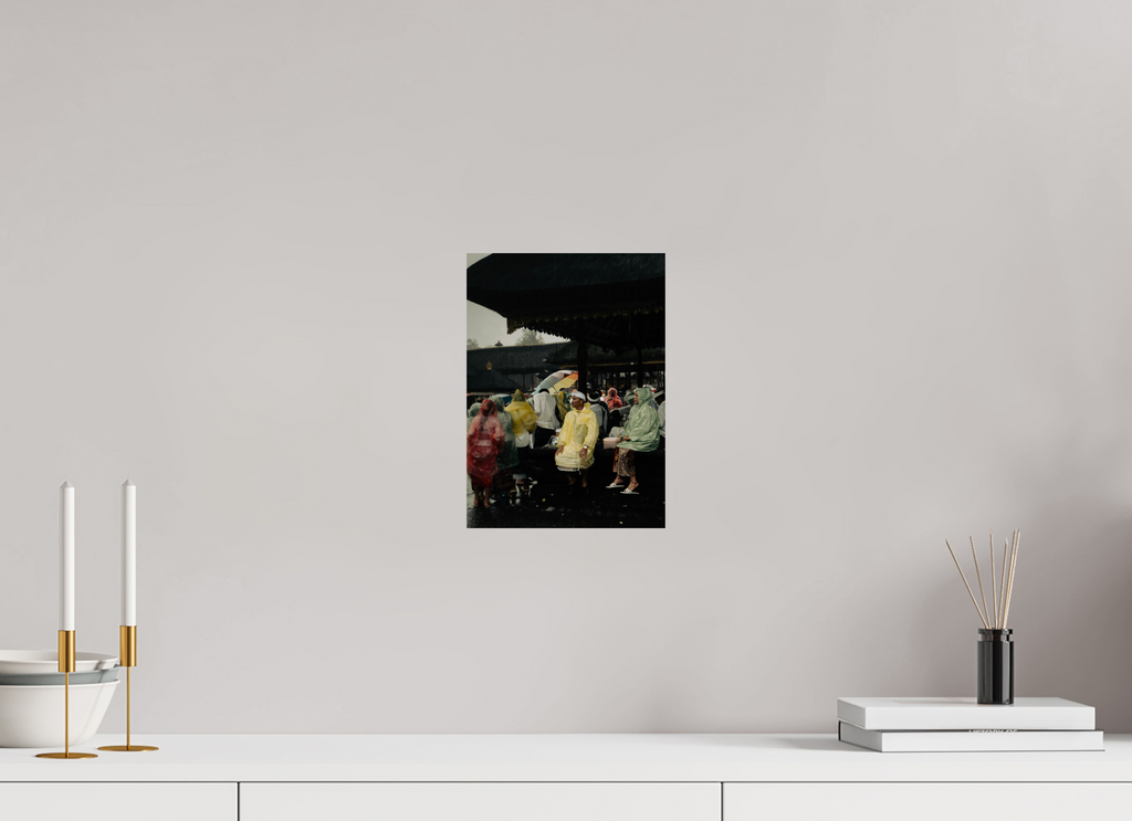 Unframed artwork on a wall above a white surface with decorative items. Focuses on people sitting out the rain at a temple on ceremony day.
